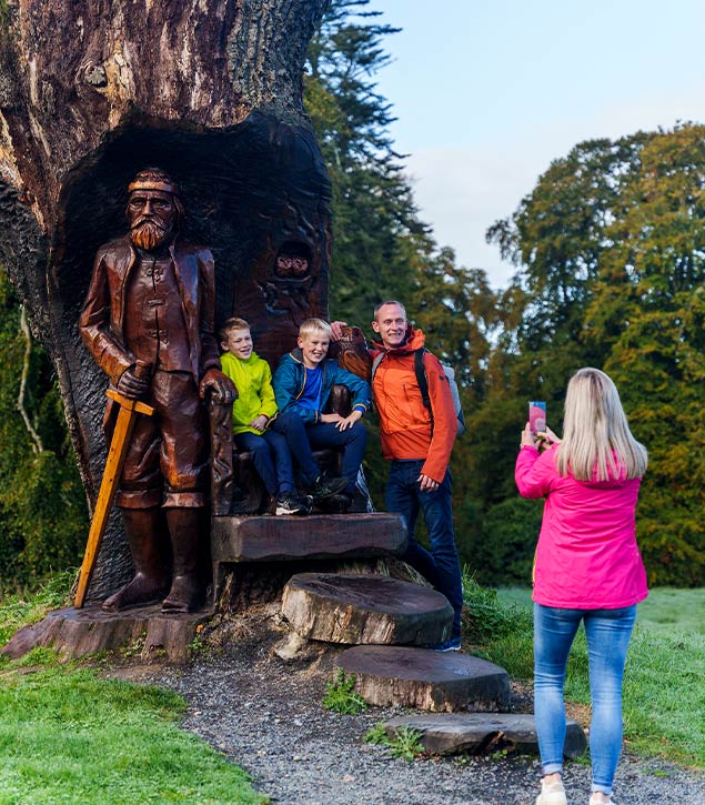 Family posing for picture by carved wooden statue.